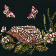 Close-up of embroidered brown hedgehog among pink blossoms, green ferns and butterflies