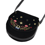 Angled view of Fable England black velvet saddle bag showing curved flap, floral embroidery and shoulder strap
