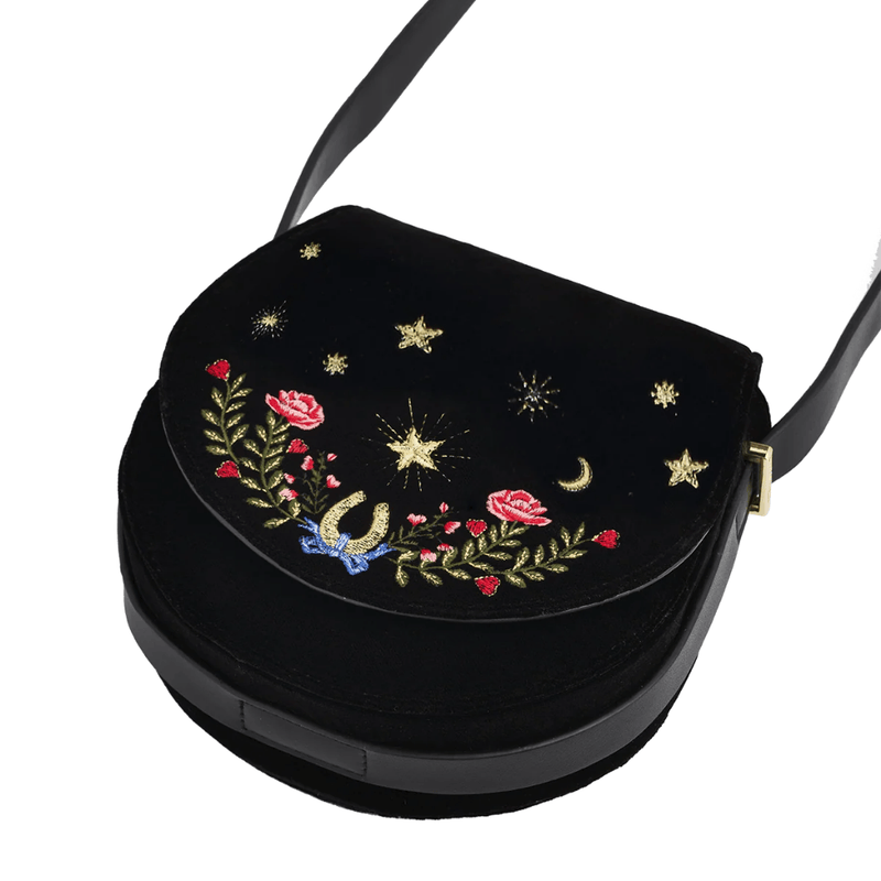 Angled view of Fable England black velvet saddle bag showing curved flap, floral embroidery and shoulder strap