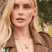 Model wearing Fable England red blossom and pomegranate earrings outdoors with a brown coat