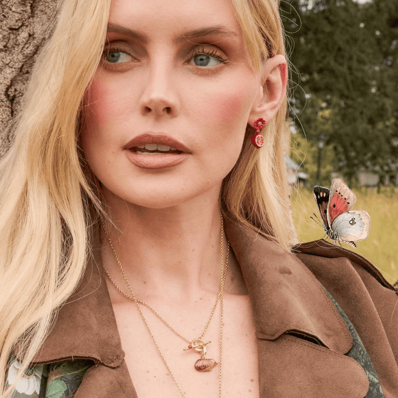 Model wearing Fable England red blossom and pomegranate earrings outdoors with a brown coat