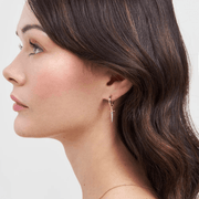 Model wearing gold Rose and Dagger Huggie Earrings with miniature dangling dagger charms