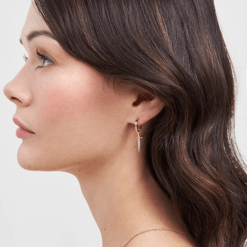 Model wearing gold Rose and Dagger Huggie Earrings with miniature dangling dagger charms