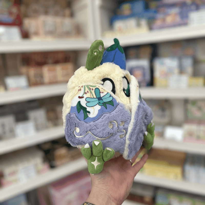 Mini Squishable Fairy Baby Mothman plush toy held in store, showing its soft fluffy body, patterned wings and cute fairy design