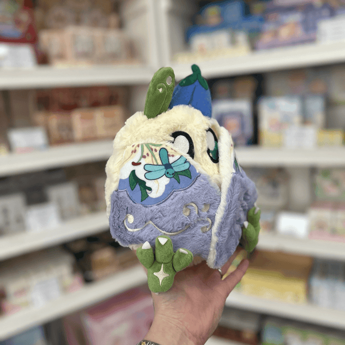 Mini Squishable Fairy Baby Mothman plush toy held in store, showing its soft fluffy body, patterned wings and cute fairy design