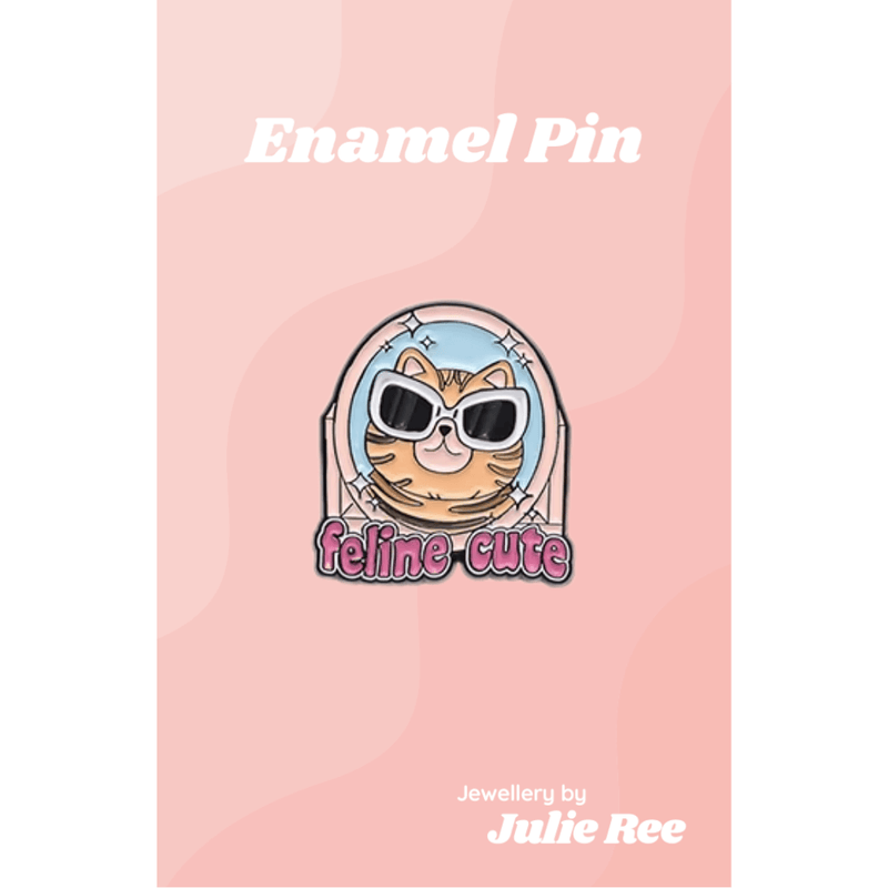 Cute enamel pin of a tabby cat wearing sunglasses with the words Feline Cute, displayed on a pink backing card.