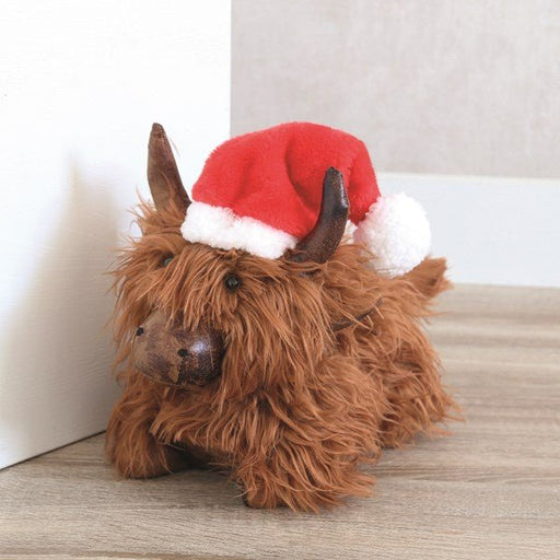 Highland cow doorstop wearing a Santa hat positioned by a door, lifestyle setting.