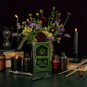 Frankenstein book vase filled with flowers on a gothic tabletop with candles and apothecary bottles.