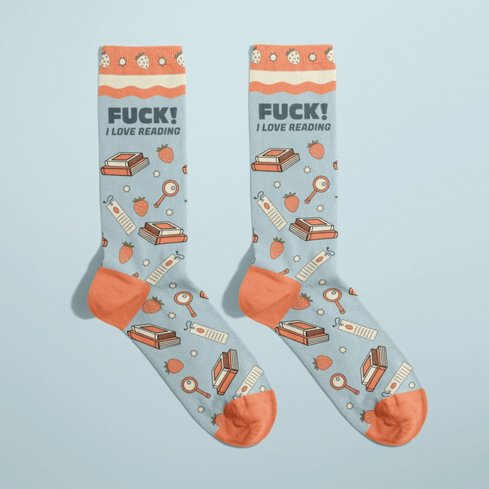Pair of light blue women’s novelty crew socks with orange accents, stacks of books and bookmarks print, bold Fuck! I love reading text at the cuff.