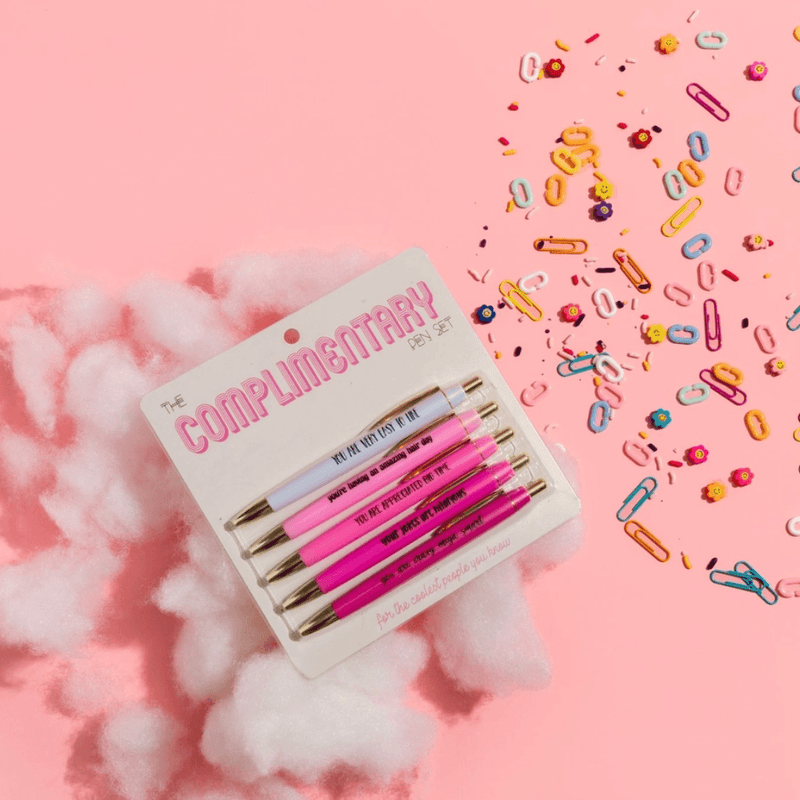 Fun Club Complimentary Pen Set styled on a pink background with fluffy white clouds, colourful paperclips and 5 compliment-themed novelty pens