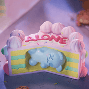 Pastel layer cake saying ALONE with blue Ghost Bear buried inside—“Sad B-day Cake” collectable
