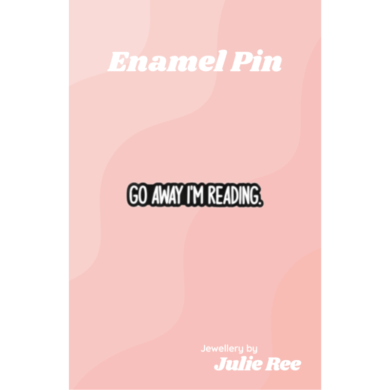 Black enamel pin with white text reading Go Away I’m Reading, displayed on a pink backing card.