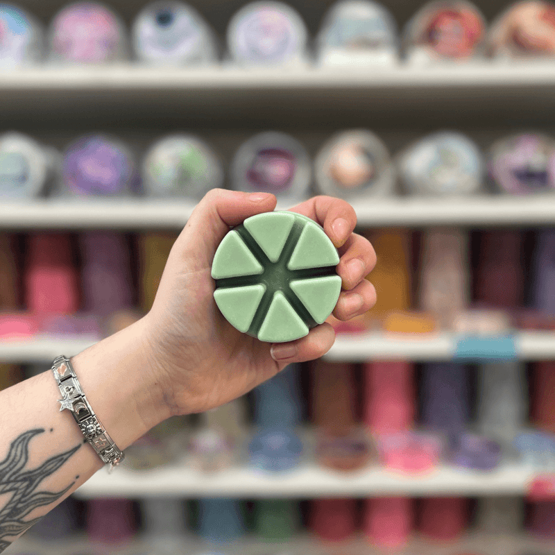 Green with Envy wax melt segments held in hand with colourful wax melt display in the background