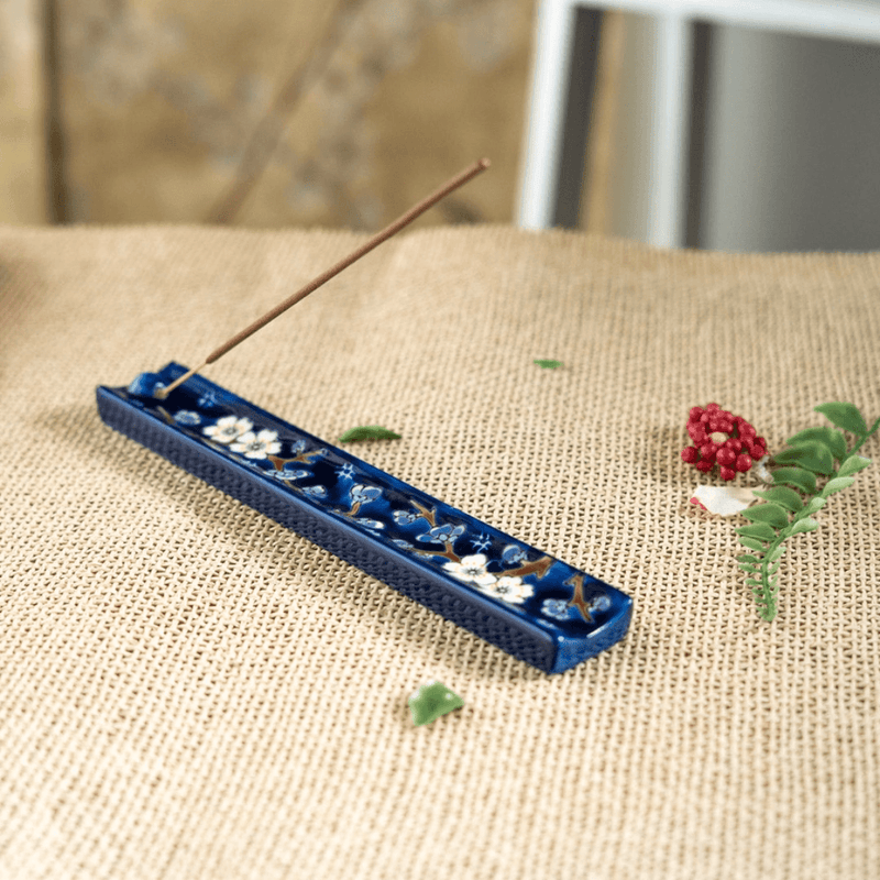 Handpainted ceramic Plum Blossom incense holder with stick incense on a woven surface
