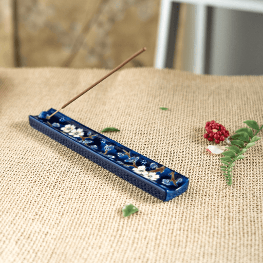 Handpainted ceramic Plum Blossom incense holder with stick incense on a woven surface