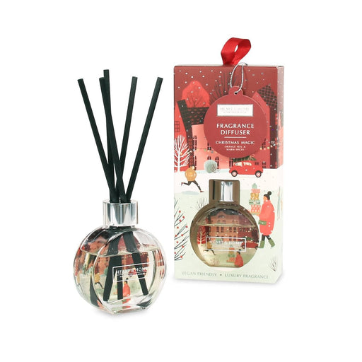 Heart & Home Christmas Magic reed diffuser in a round glass with black reeds next to the illustrated red gift box with hanging ribbon tag.