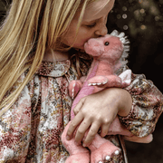 Child cuddling Hearts pink dragon plush from Bearhouse by Charlie Bears 2025, showing soft plush face, horns and fluffy mane