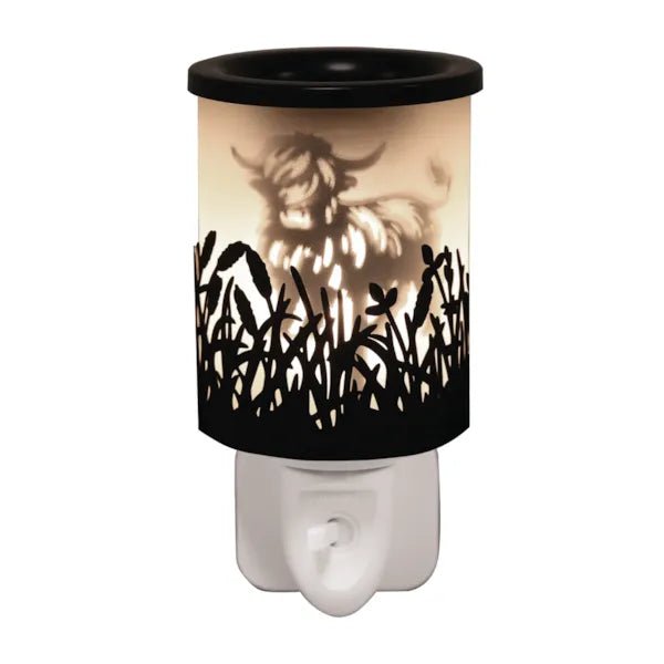 Black plug in wax melt burner glowing with a Highland cow silhouette and cut-out grass detail, with an on/off switch on the plug base.