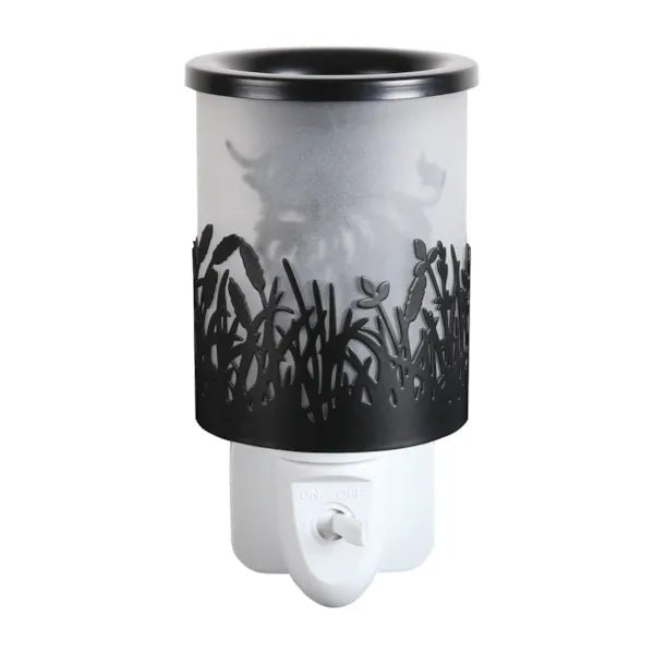 Black plug in wax melt burner unlit with frosted panel and cut-out grass design, showing the Highland cow silhouette in the background.