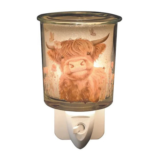 Highland cow glass plug in wax melt burner switched on, glowing warmly through the illustrated countryside design.