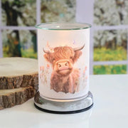 Highland cow touch wax melt burner styled on a tabletop with a softly lit countryside design.