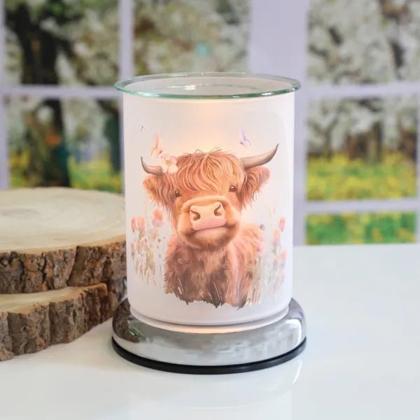 Highland cow touch wax melt burner styled on a tabletop with a softly lit countryside design.