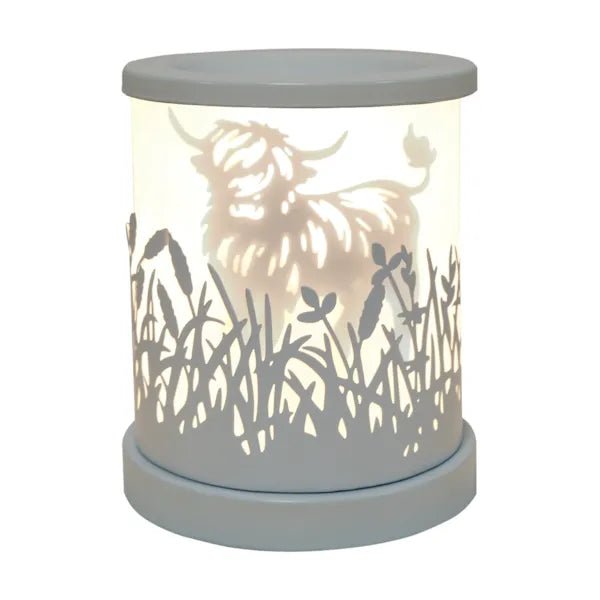 White Highland cow silhouette electric wax melt burner glowing warmly with meadow cut-out detailing.