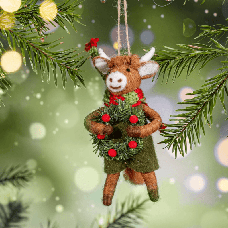 Highland cow holding a festive wreath felt decoration hanging on a Christmas tree