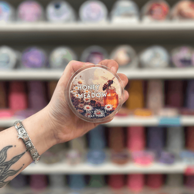Honey Meadow wax melt pot held in hand with colourful wax melt display in the background