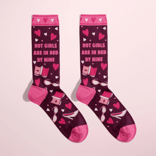 Women’s burgundy crew socks with pink heels, hearts and bedtime icons, text Hot girls are in bed by nine, on pink background.