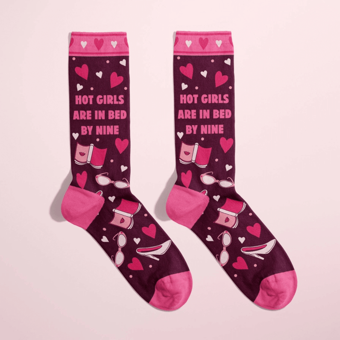 Women’s burgundy crew socks with pink heels, hearts and bedtime icons, text Hot girls are in bed by nine, on pink background.