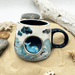 Lifestyle photo of the cup on sand with shells, showing the 3D whale detail on the front