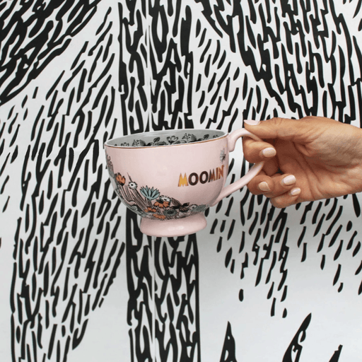 House of Disaster Moomin Love porcelain cup held in hand showing pink exterior, floral design and gold Moomin logo