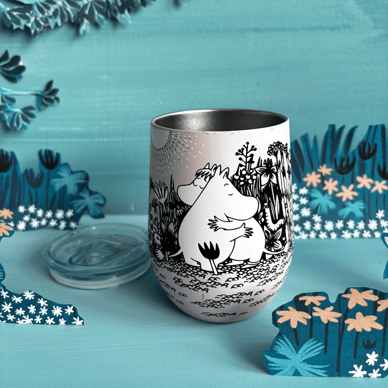 Front lifestyle view of open House of Disaster Moomin Love keep cup with lid beside the tumbler in a blue floral scene