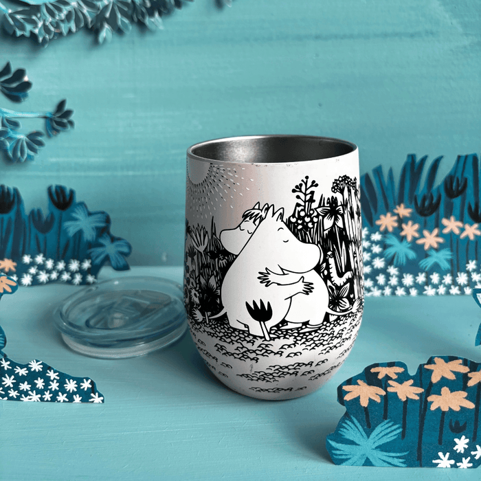Front lifestyle view of open House of Disaster Moomin Love keep cup with lid beside the tumbler in a blue floral scene