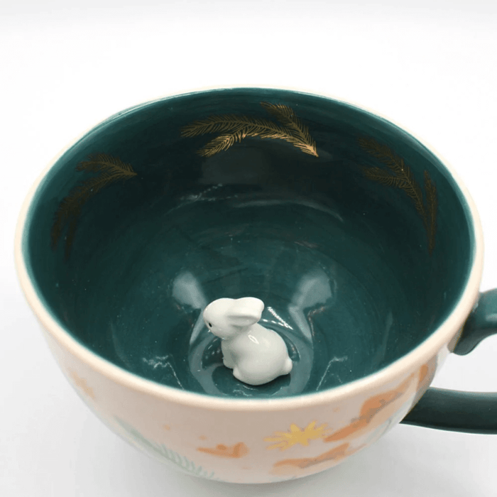 Close-up inside the cup showing the small ceramic rabbit and gold leaf details on teal glaze