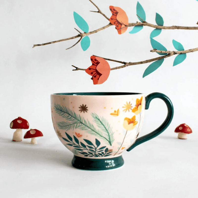 Lifestyle photo of the cup on a table with floral styling and teal handle visible