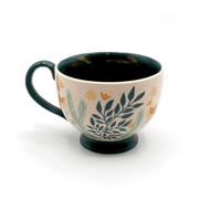Side view of the porcelain teacup with foliage print, soft pink glaze and teal handle