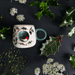 Flatlay of the Robin Cup with festive greenery, featuring the 3D robin nook on the front