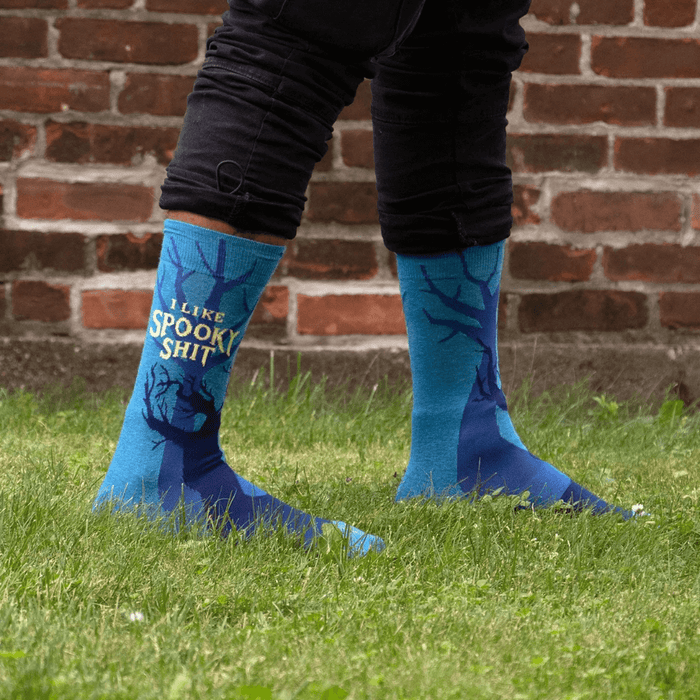 Person wearing I Like Spooky Shit men’s socks outdoors, blue spooky tree design.