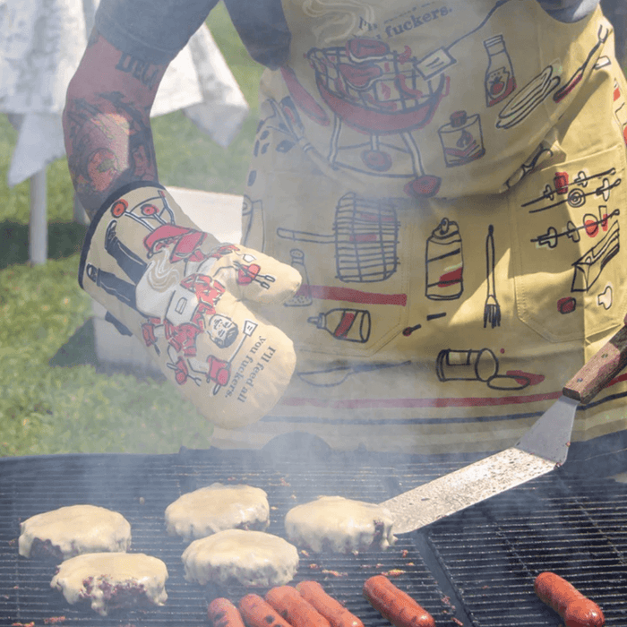 BBQ cooking scene with novelty oven mitt and burgers on grill.
