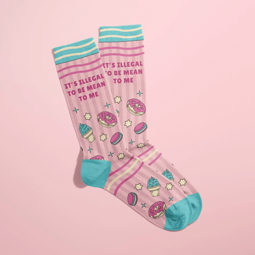 Pink women’s crew socks with teal heels and cuffs, dessert icons and stars, slogan “It’s illegal to be mean to me,” shown overlapped on pink backdrop.