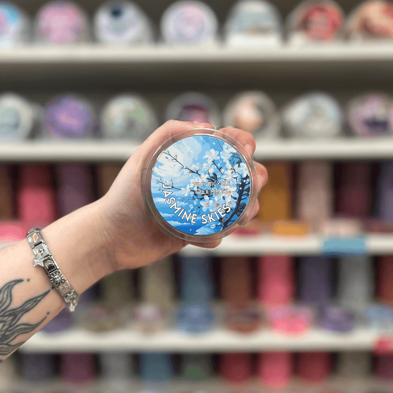 Jasmine Skies wax melt pot held in hand with colourful wax melt display in the background