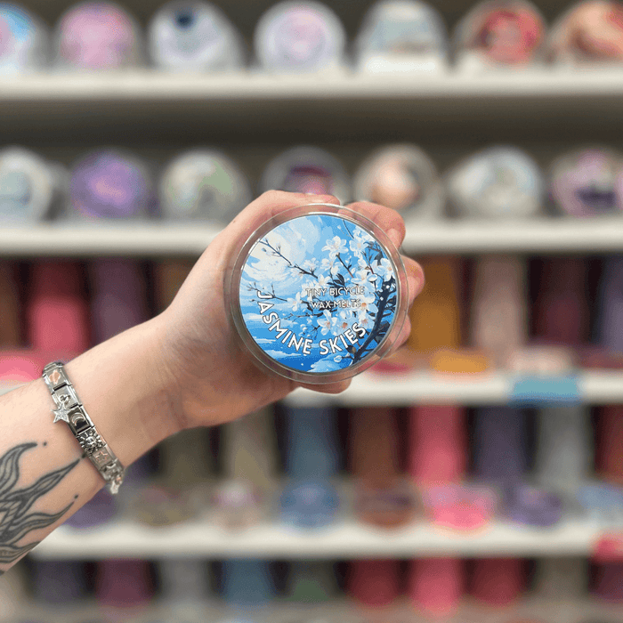Jasmine Skies wax melt pot held in hand with colourful wax melt display in the background