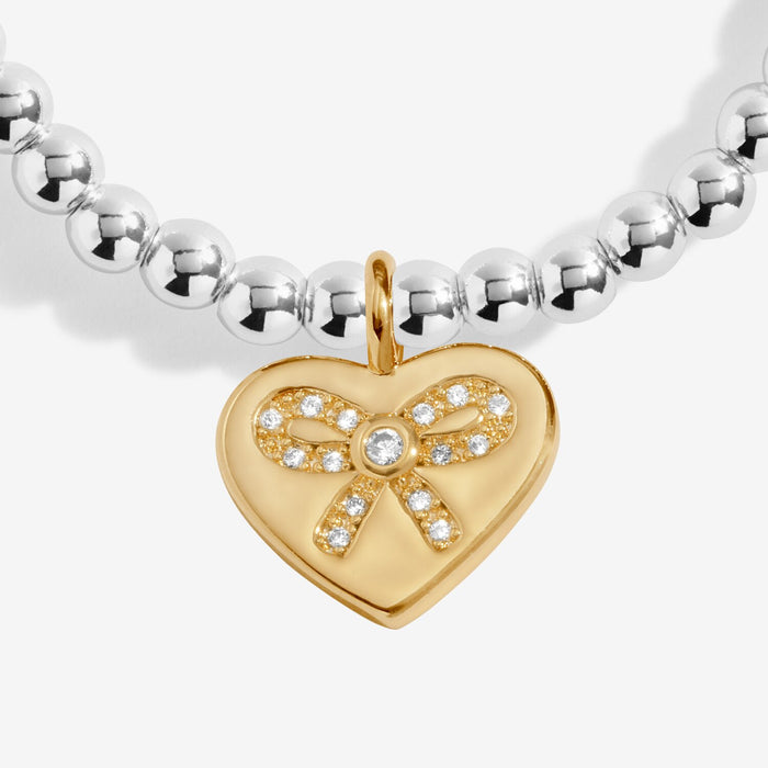 Close-up of Joma A Little Bestie Birthday Bracelet charm, gold heart with bow and crystal detail.