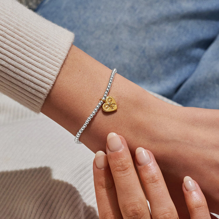 Joma A Little Bestie Birthday Bracelet worn on wrist, silver-plated beads with gold heart bow charm.