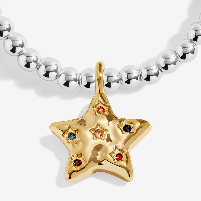 Close-up of gold-plated star bracelet charm with colourful stone accents