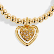 Close-up of Joma Jewellery gold open heart frame with a sparkly heart charm on a gold-plated beaded Bracelet.