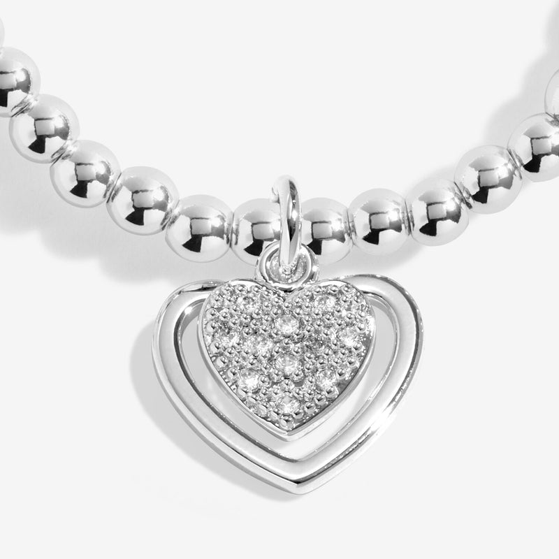 Close-up of Joma Jewellery charm with a sparkly heart inside an open heart frame on a silver-plated beaded Bracelet.