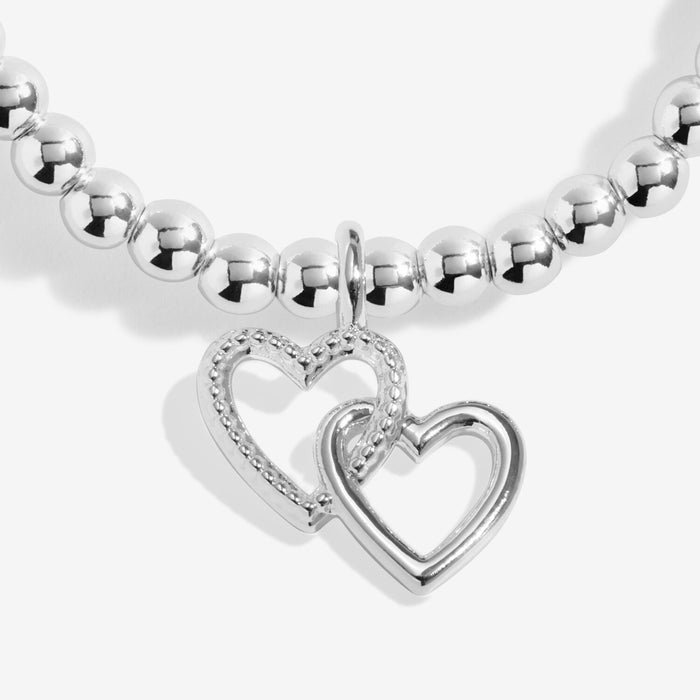 Close-up of two interlinked open heart charms on silver-plated beaded stretch Bracelet